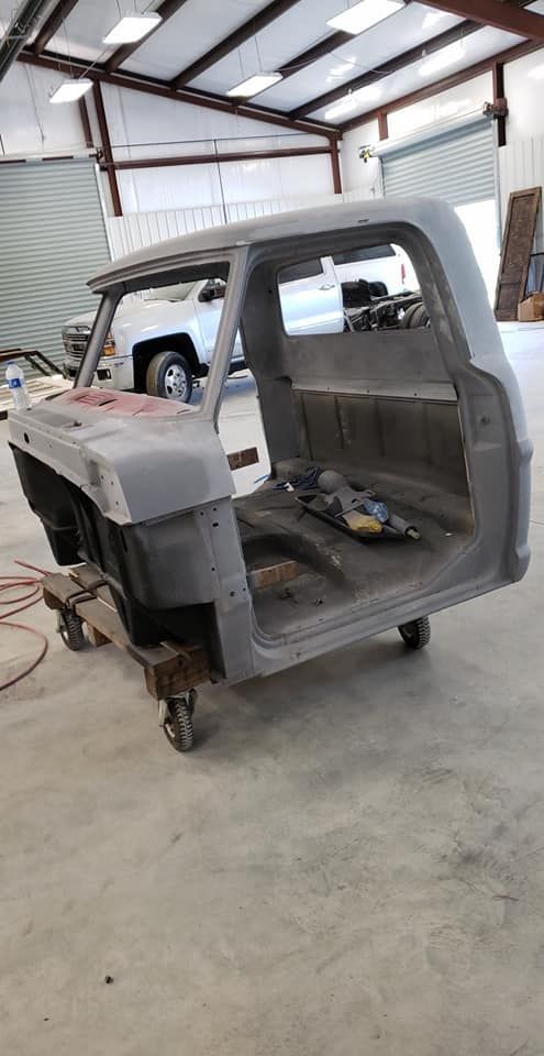 Partially stripped truck cab in a workshop, with exposed metal frame and missing front body panels