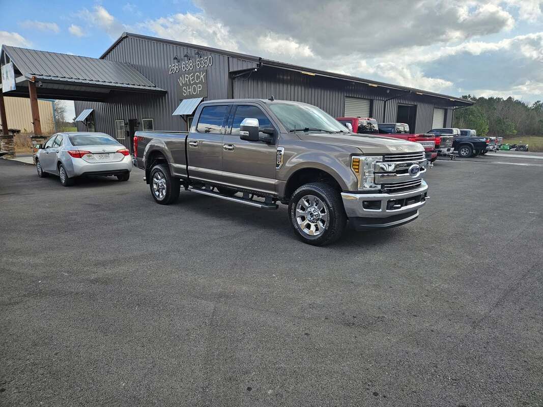 Silver pickup truck parked in a lot near a building, with cars in the background