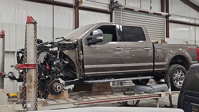 Damaged gray pickup truck on a frame straightening machine in an auto repair shop