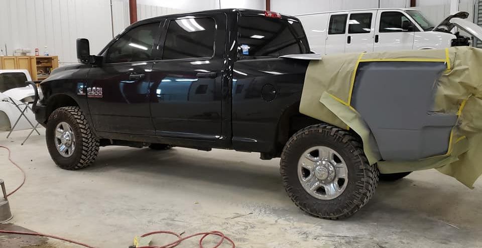 Black pickup truck in a workshop with rear quarter panels covered in gray primer and masking tape