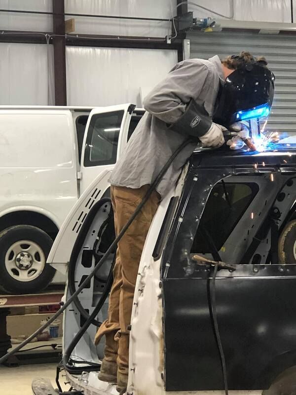 Technician welding on a black car inside an auto repair shop, with a white van in the background