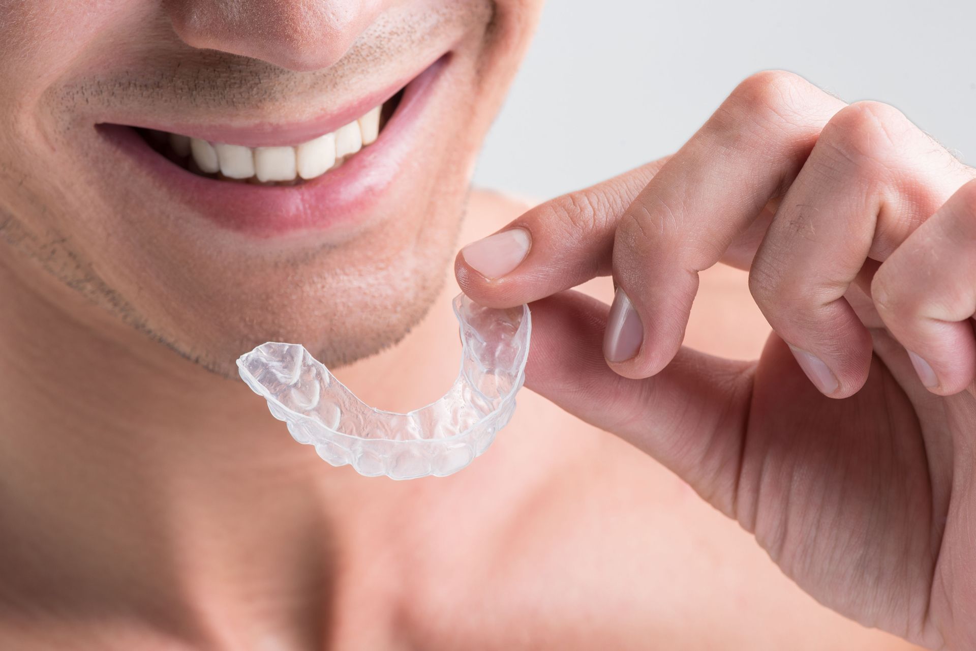 a man is smiling while holding a clear retainer in his hand