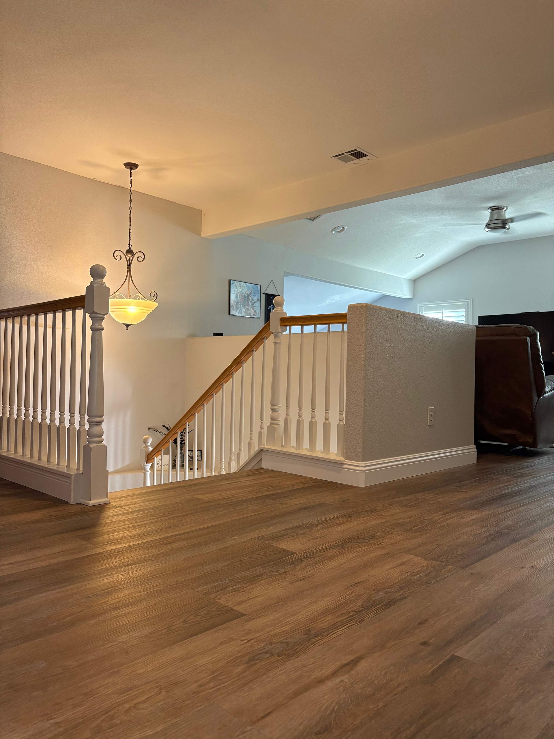 Wooden staircase in a home with white railing and brown flooring. A chandelier hangs overhead.