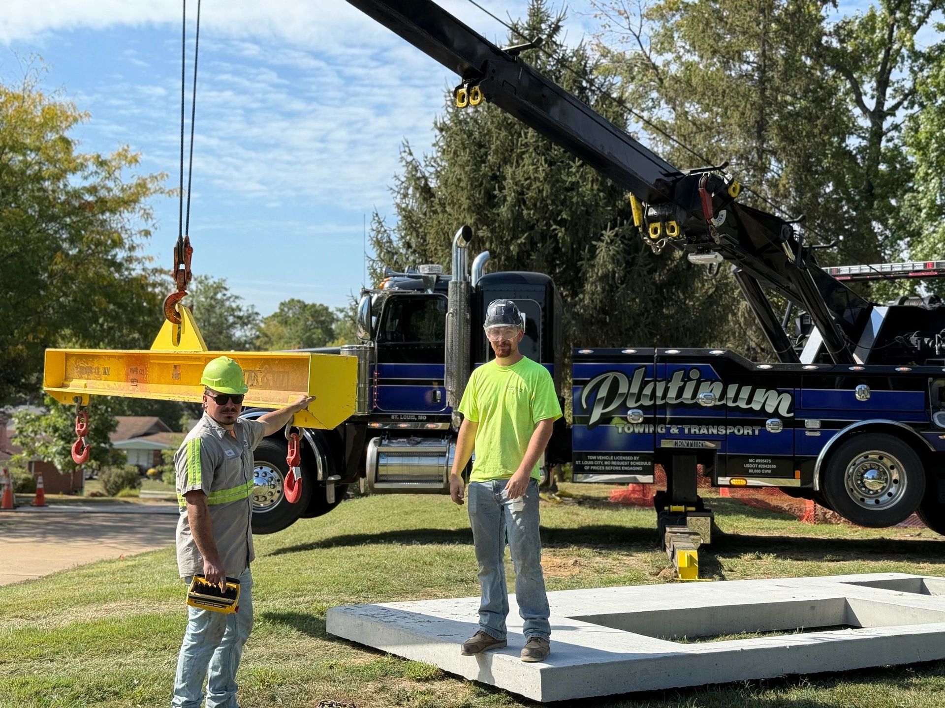 Two workers with a tow truck lift a large concrete slab. One points, the other stands nearby.