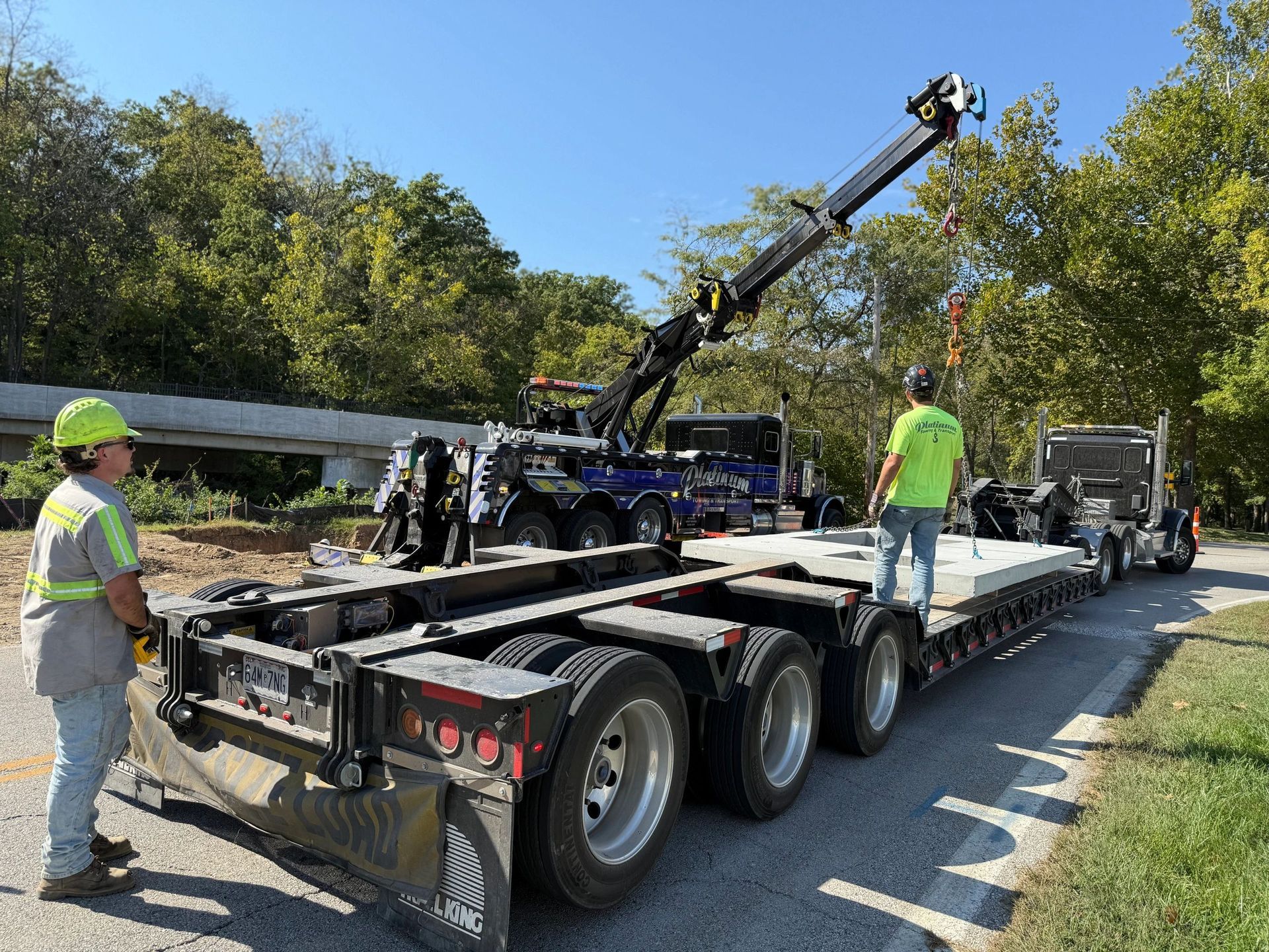 Two workers with a truck crane lift a large concrete slab on a highway.