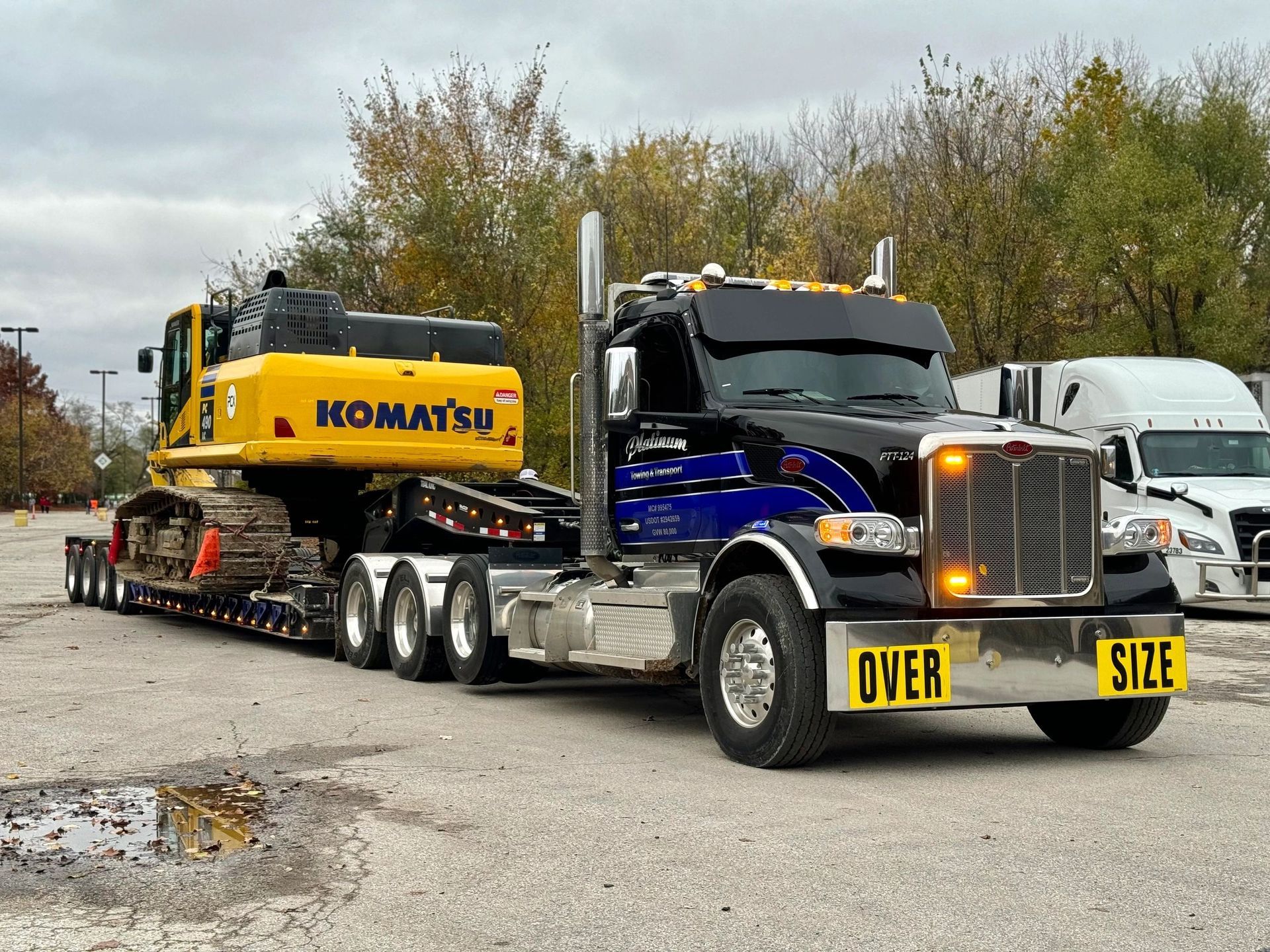 Yellow Komatsu excavator on flatbed trailer pulled by a Peterbilt semi-truck labeled 