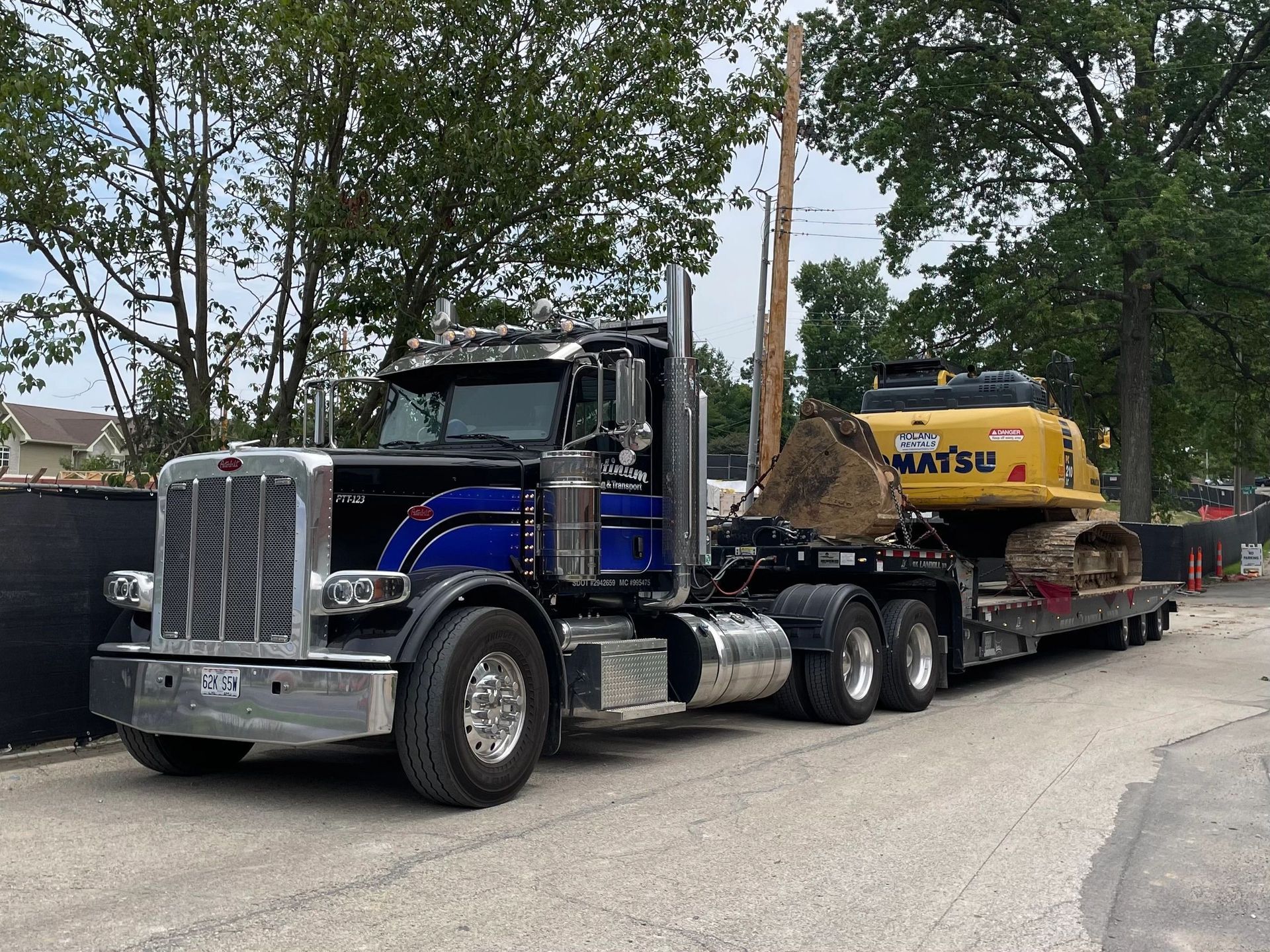 Black and blue Peterbilt truck hauling a Komatsu excavator on a trailer on a road.