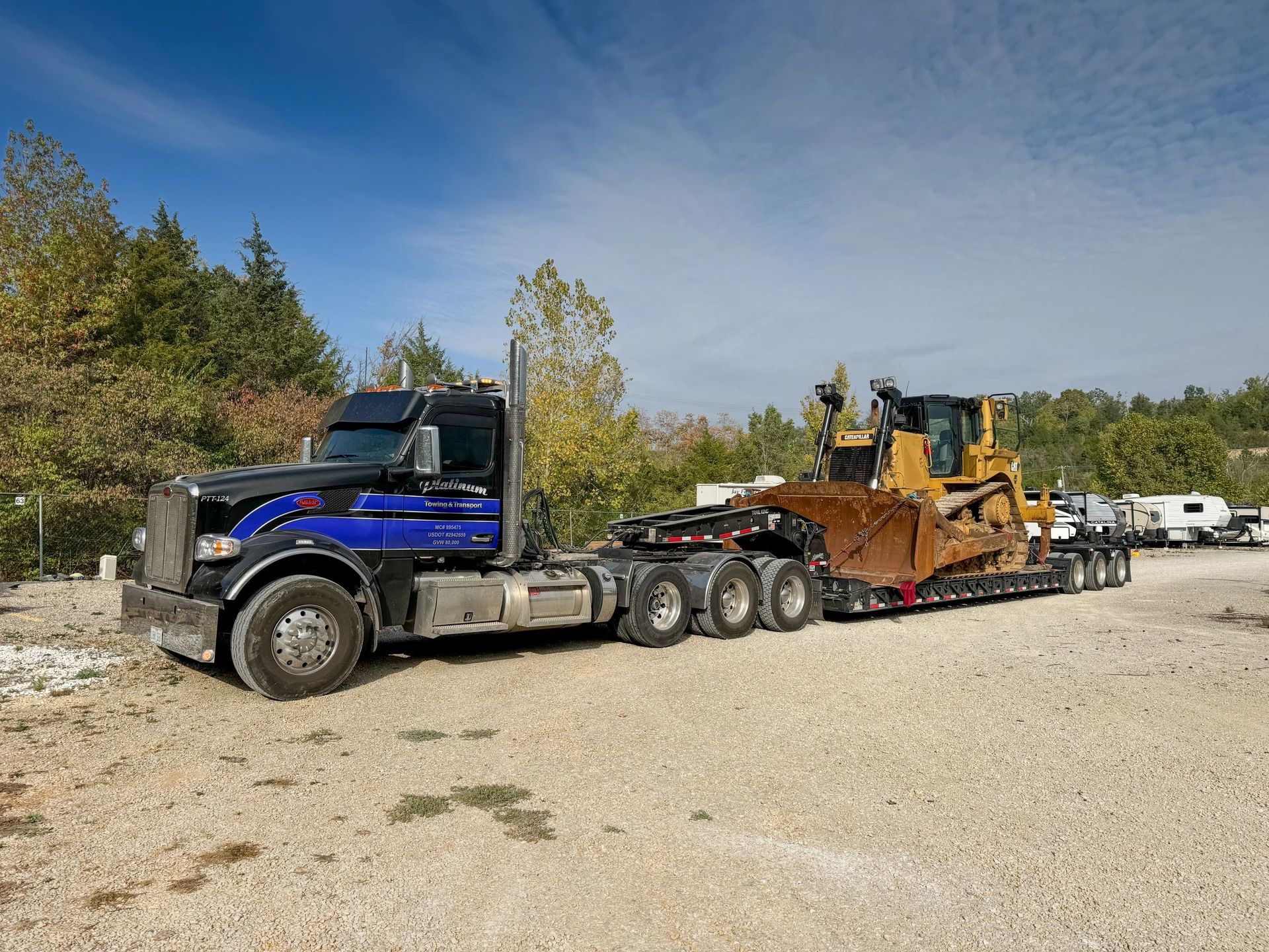 A semi-truck hauling a Caterpillar bulldozer on a trailer; parked on gravel.