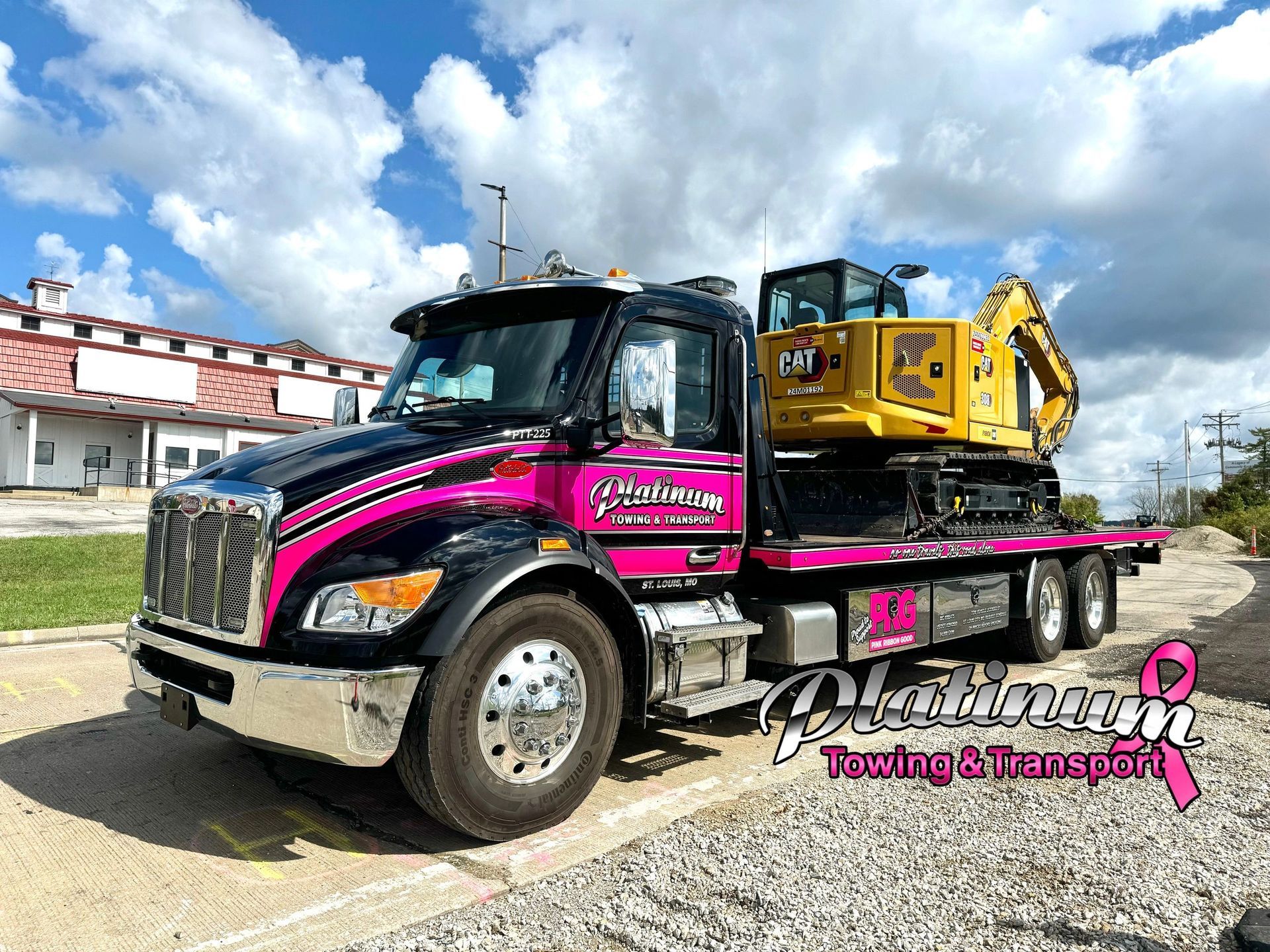 Pink and black Platinum Towing truck transporting a yellow Caterpillar excavator.