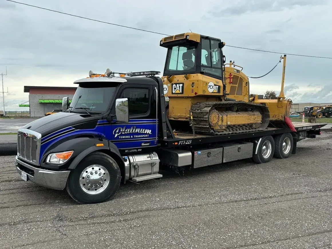 Heavy-duty tow truck hauling a yellow bulldozer on a flatbed, parked on gravel.
