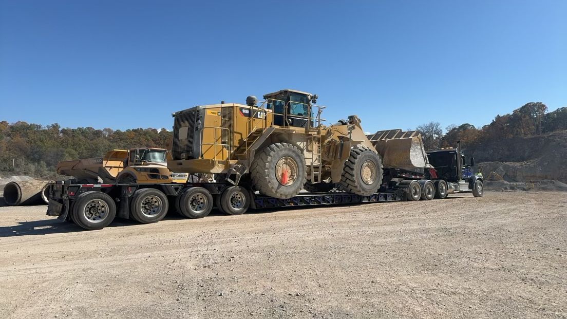 A large yellow construction vehicle is transported on a flatbed trailer on a sunny day.
