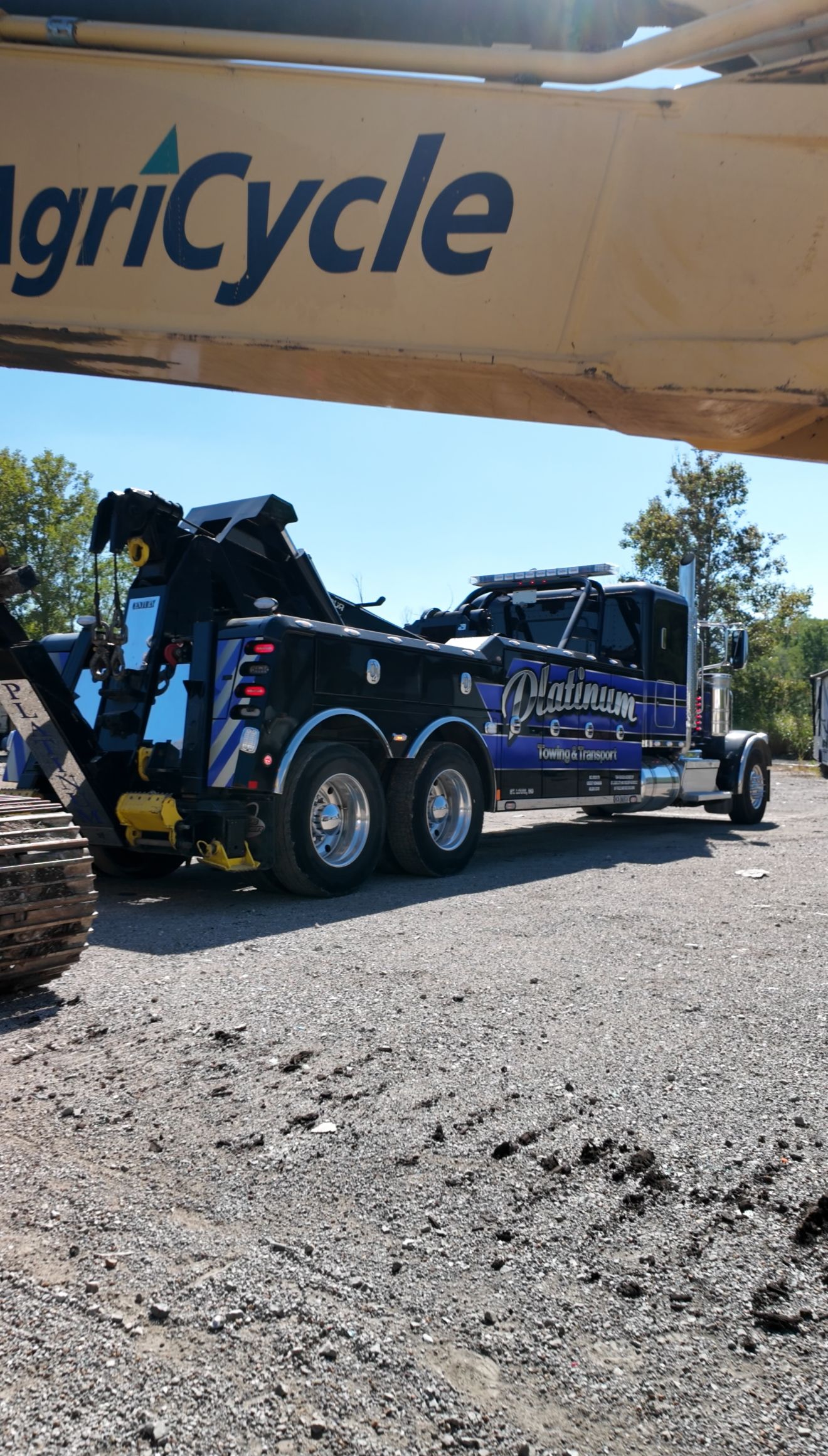 Black tow truck with Agricycle logo under blue sky, on gravel.