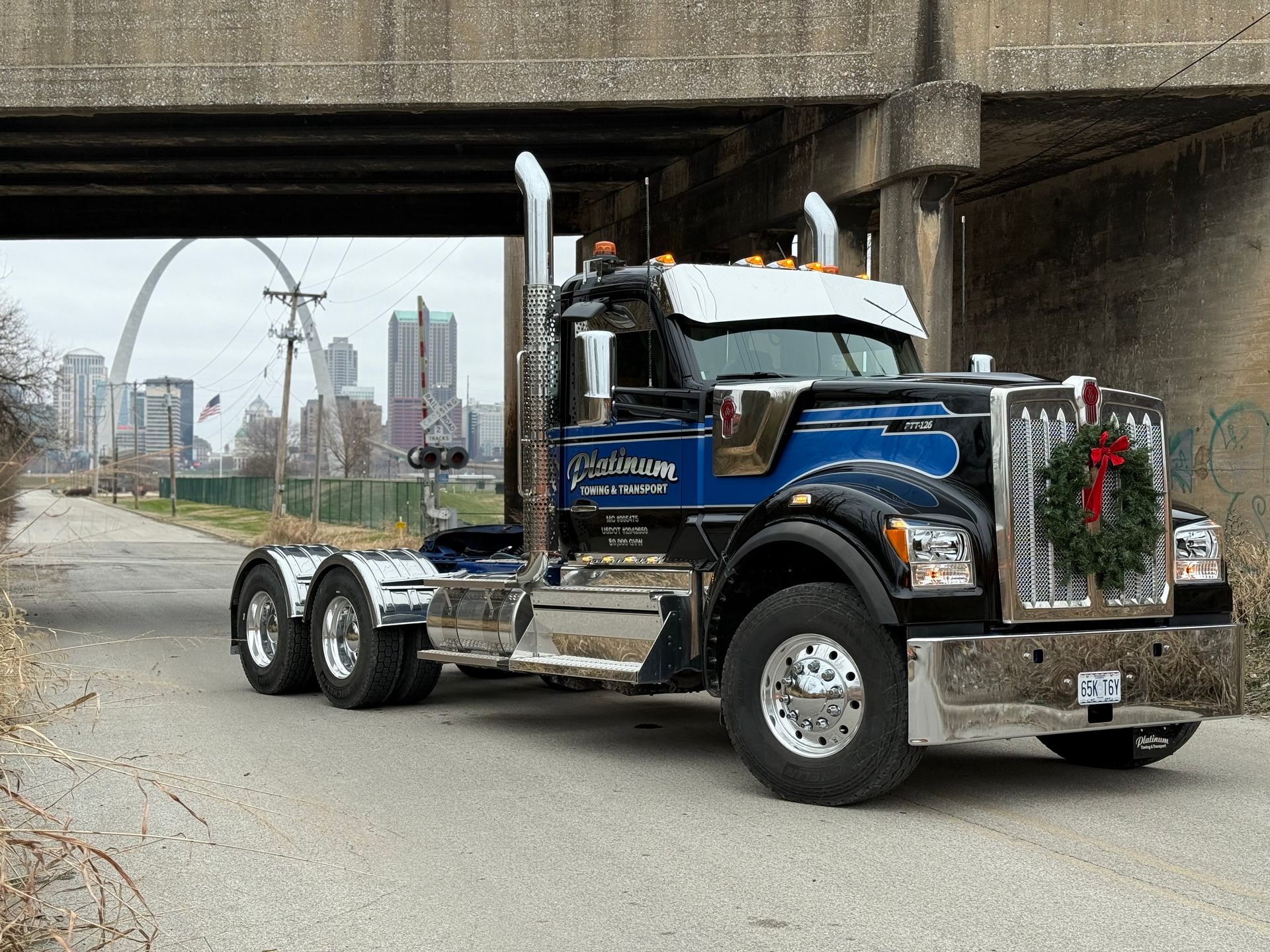 Semi-truck parked under an overpass with a Christmas wreath. St. Louis skyline with arch in the background.