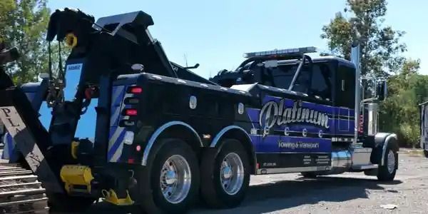 Black and blue Platinum Towing truck parked outdoors on a sunny day.