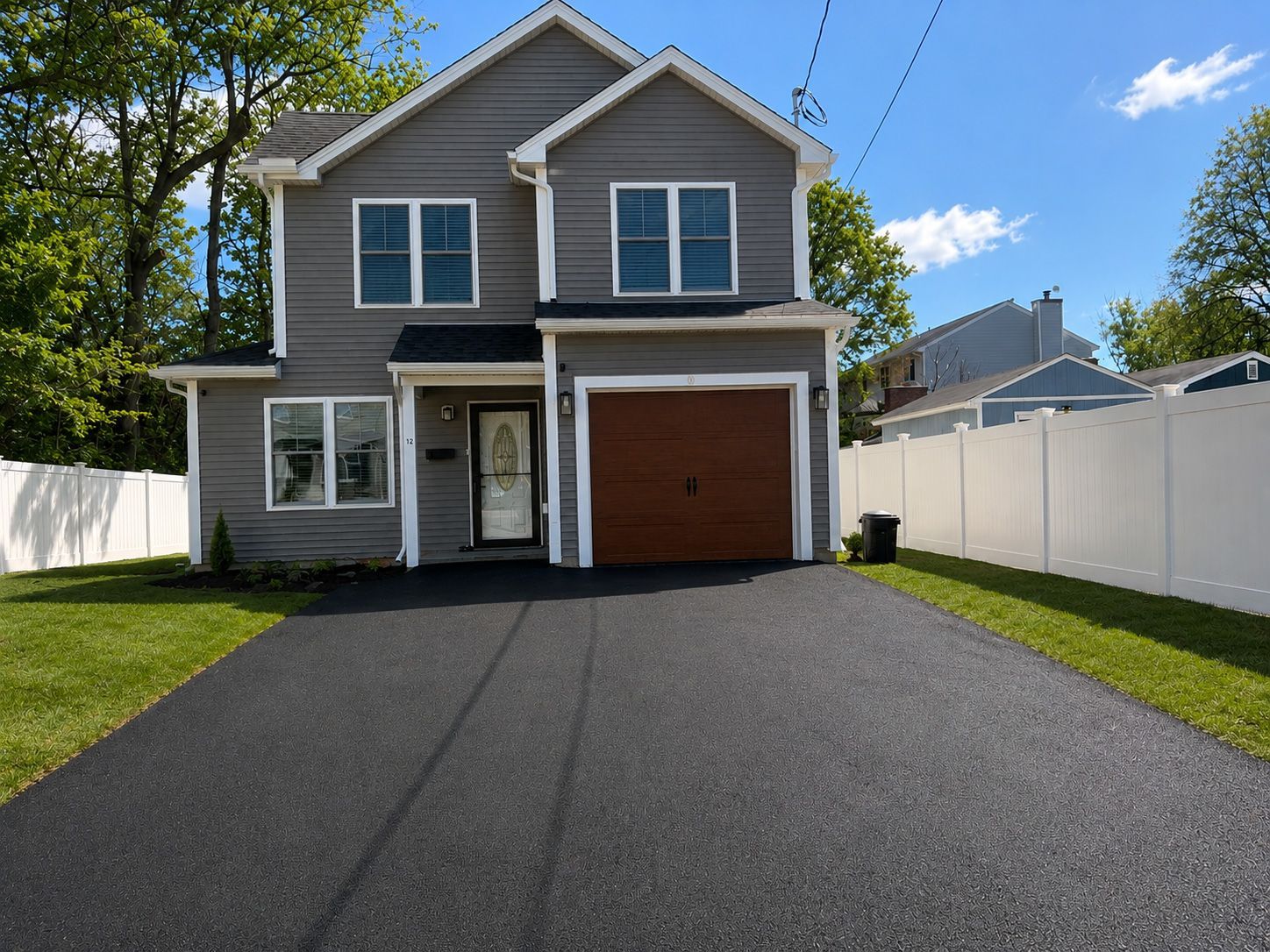 Two-story gray house with brown garage and large black driveway under a blue sky