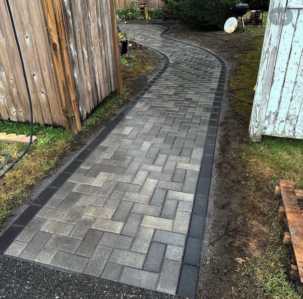 Curved gray brick walkway between wooden and white fences in a yard