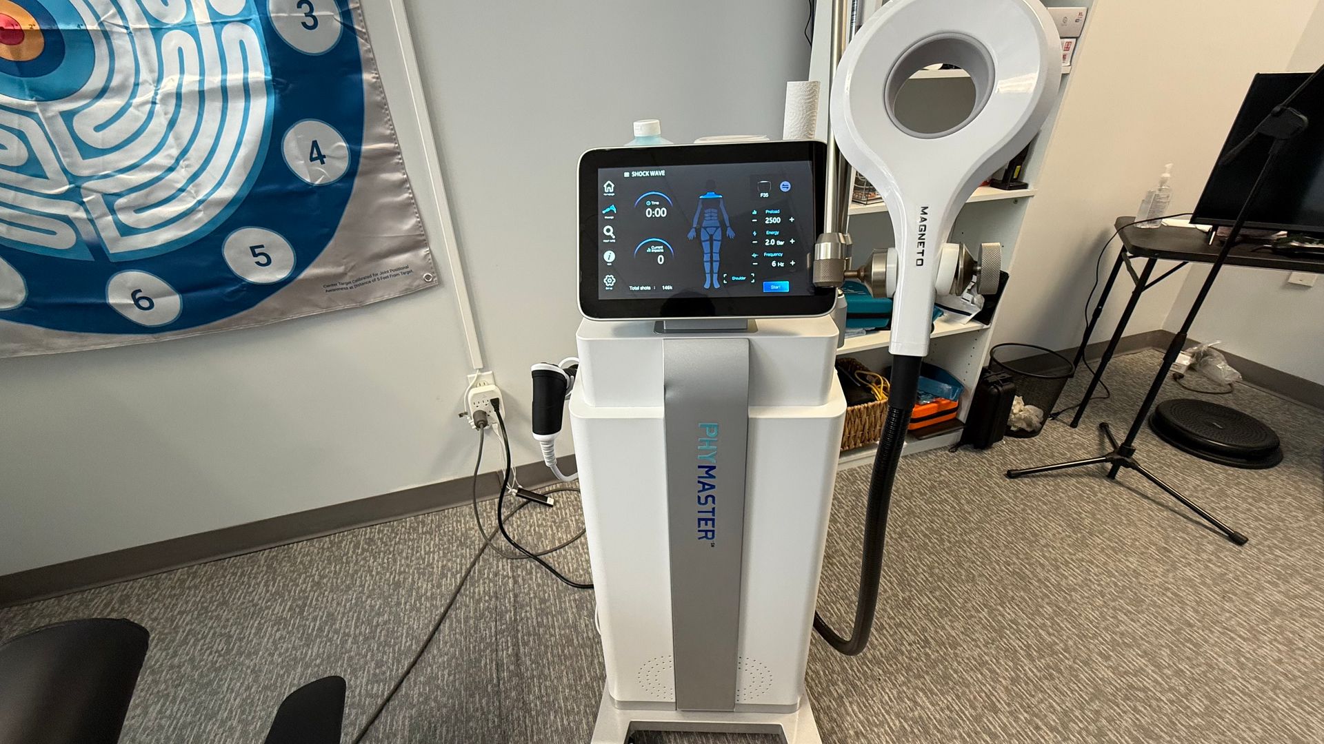 A white medical device with a screen and a large circular head. It's in a room with a rug and wall art.