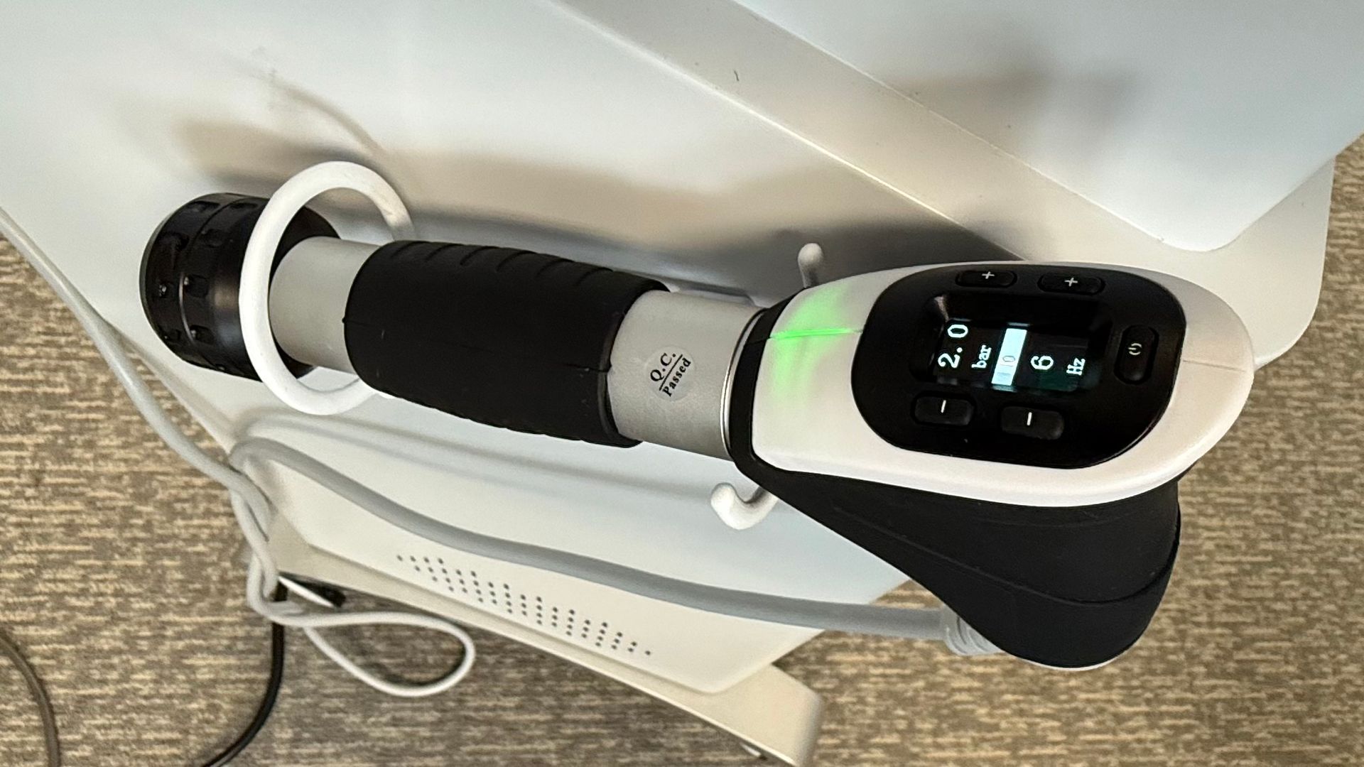 A medical device with a display and a black handle extending from a white base. A green light is on.