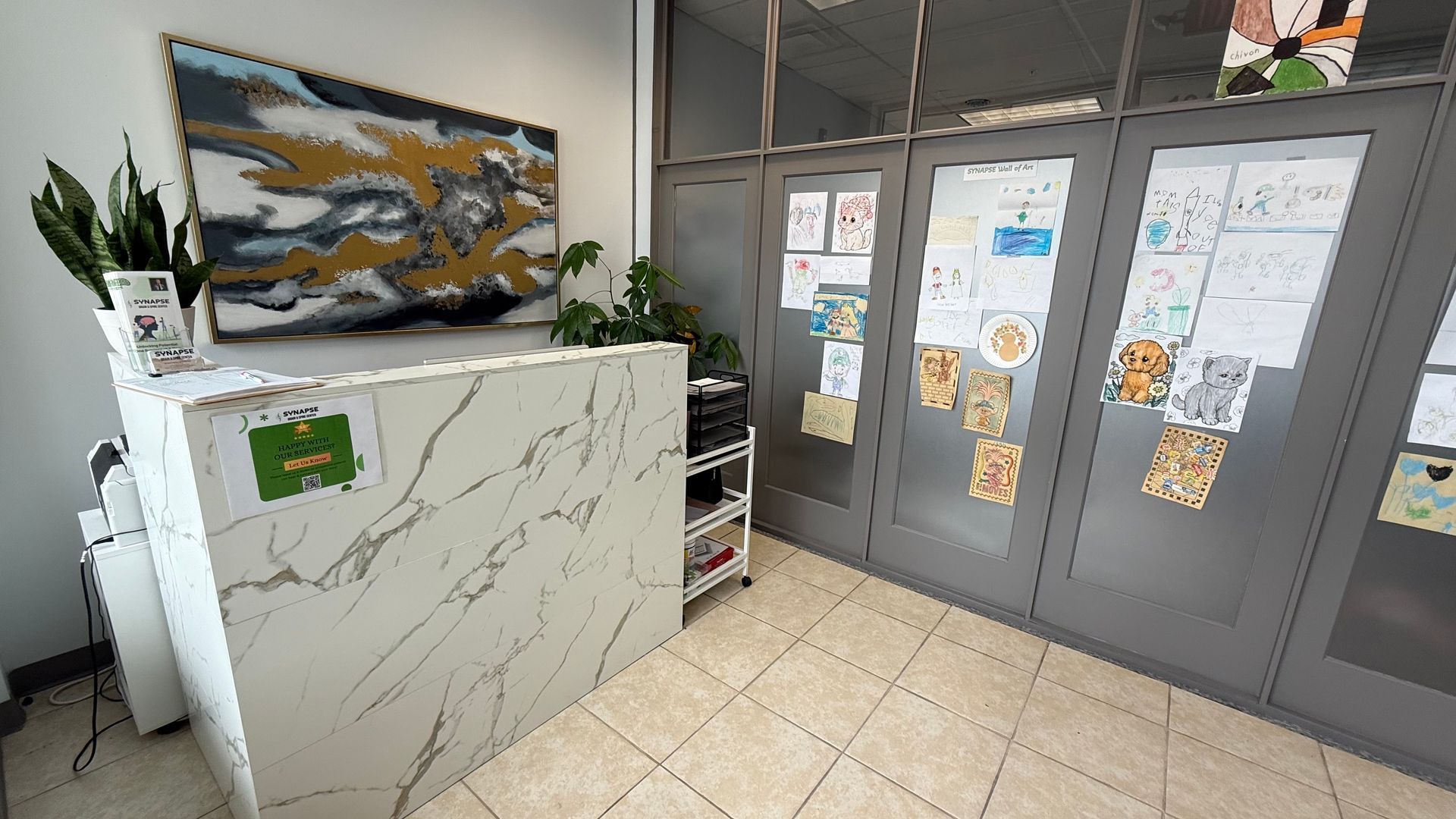 Reception desk with marble-like facade and abstract painting. Glass doors adorned with drawings and art.