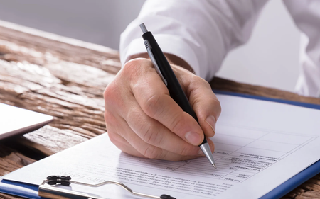A person is writing on a clipboard with a pen.