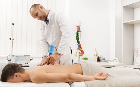 A man is lying on a bed getting a massage from a doctor.