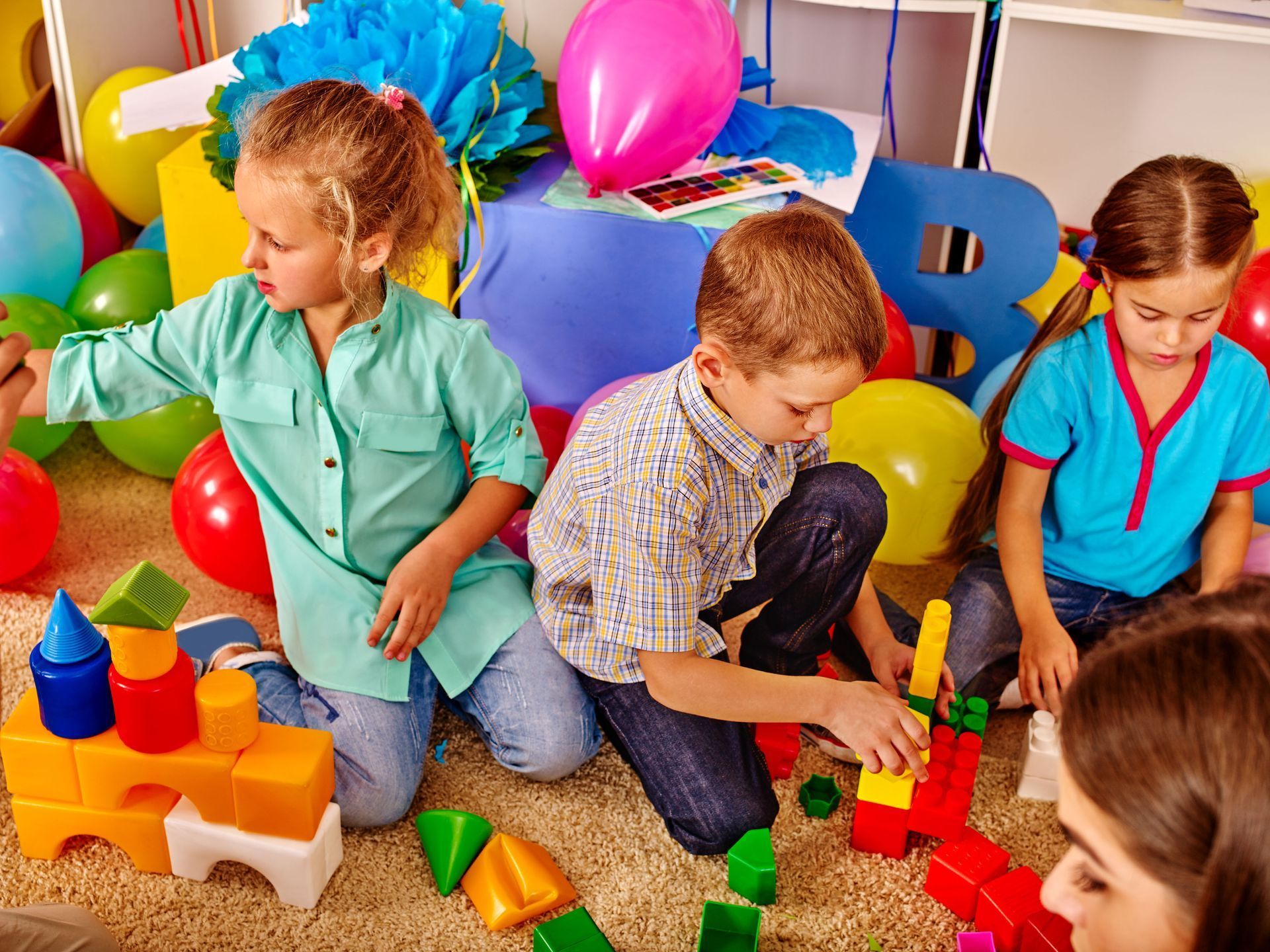 Children playing with building blocks surrounded by balloons and decorations.