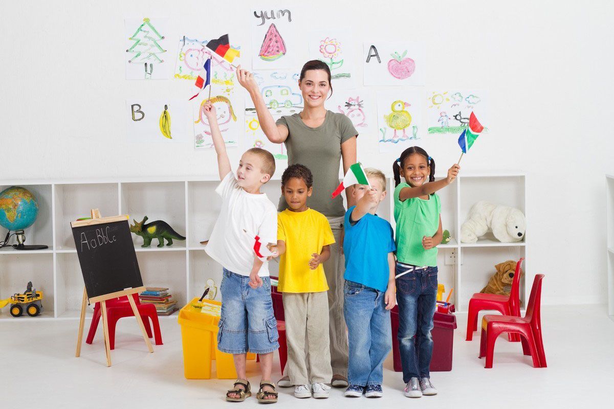Teacher and four children holding flags in a brightly decorated classroom.