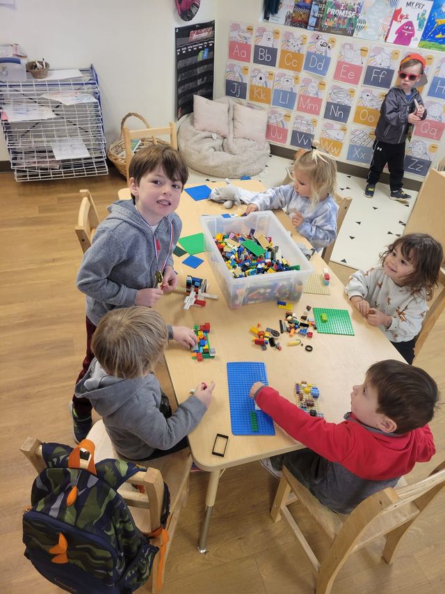 Children building with Legos at a table in a classroom. One child is wearing sunglasses.