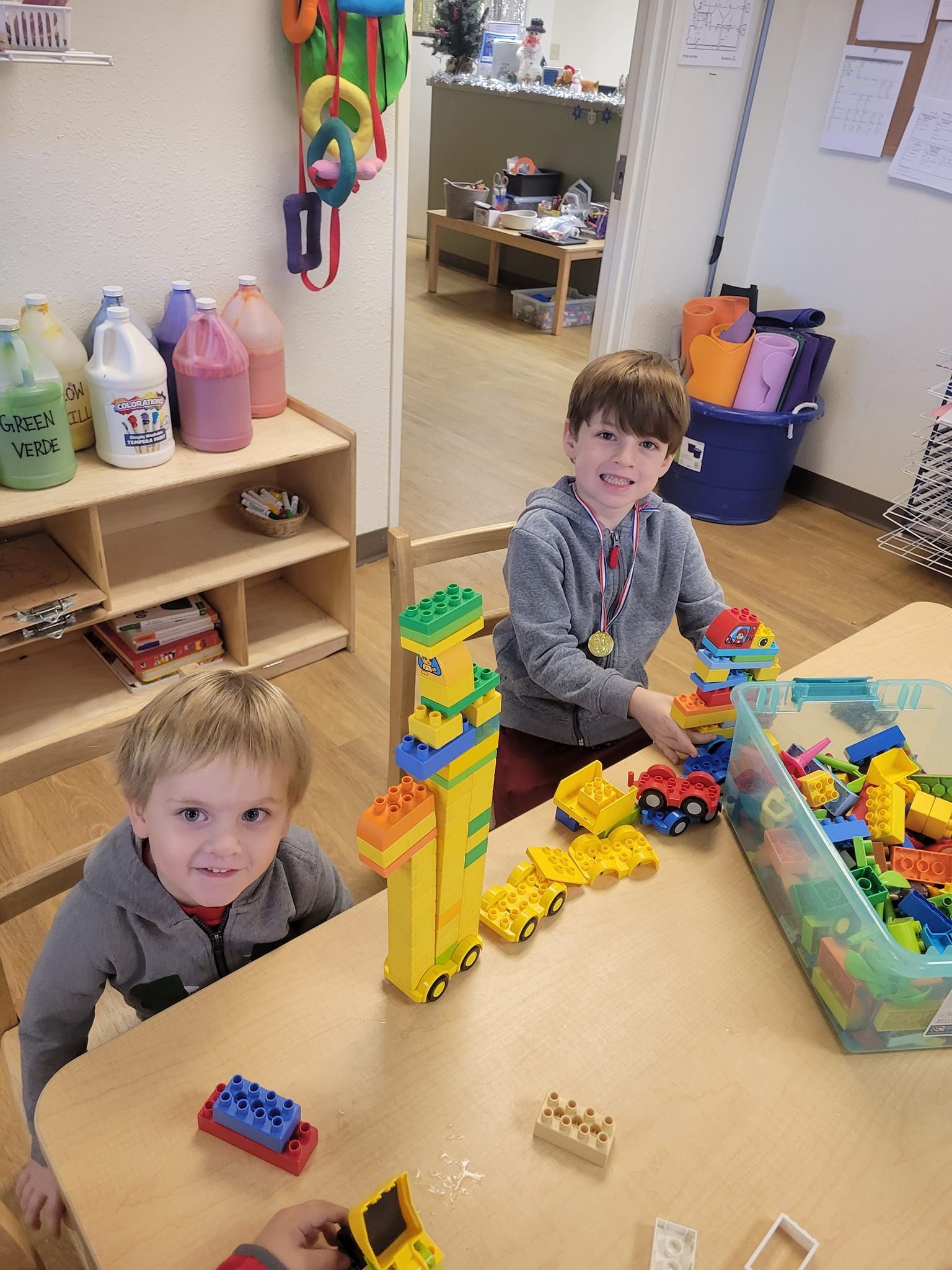 Two children playing with colorful building blocks at a table in a classroom.