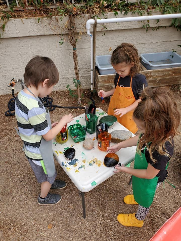 Girl with painted hands framing her face, smiling. Hands are multi-colored.