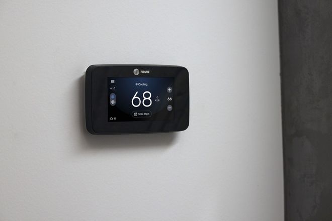 Wall-mounted digital thermostat displaying 68° on a white wall near a dark doorway