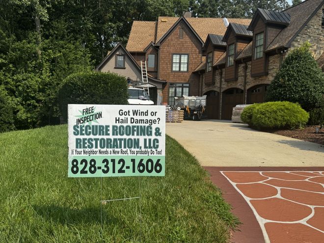 Lawn sign for Secure Roofing & Restoration LLC in front of brick townhomes with a driveway.