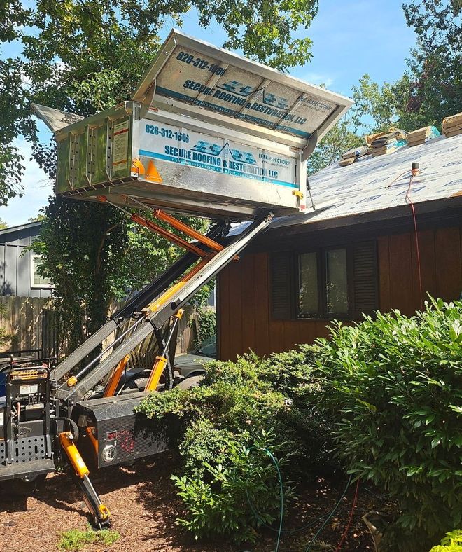 Backhoe lifting a large sign near a building, with trees and shrubs in the foreground