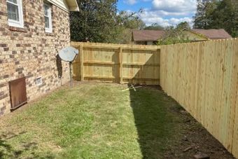A newly constructed wooden fence encloses a grassy backyard, adjacent to a brick house