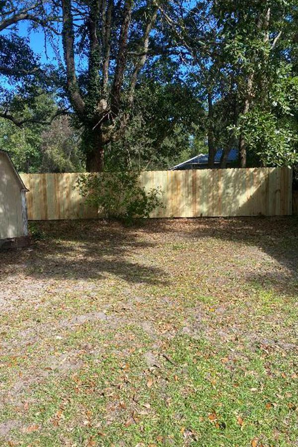 A wooden fence is surrounded by trees in a backyard.