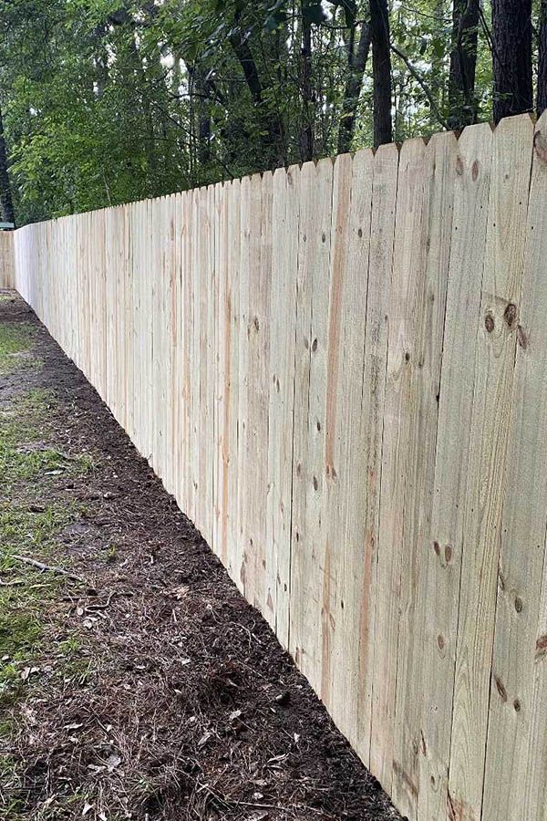 A long wooden fence is surrounded by trees and dirt.