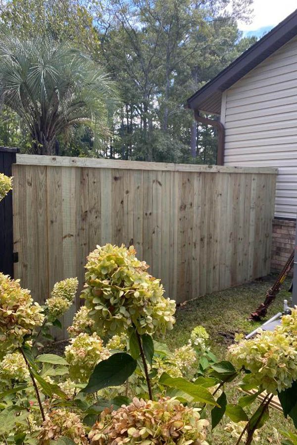 A wooden fence is surrounded by flowers in front of a house.