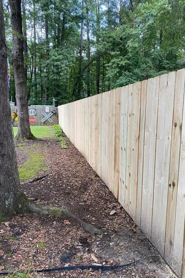 A wooden fence is surrounded by trees and a dirt path.