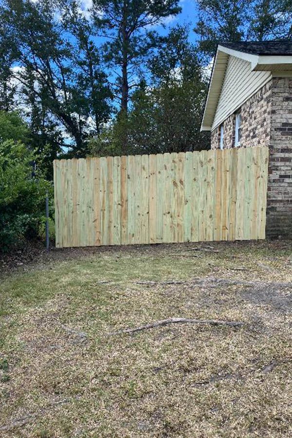 A wooden fence is sitting in front of a brick house.