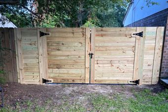 Wooden double gate in a yard, secured with black hinges and a latch