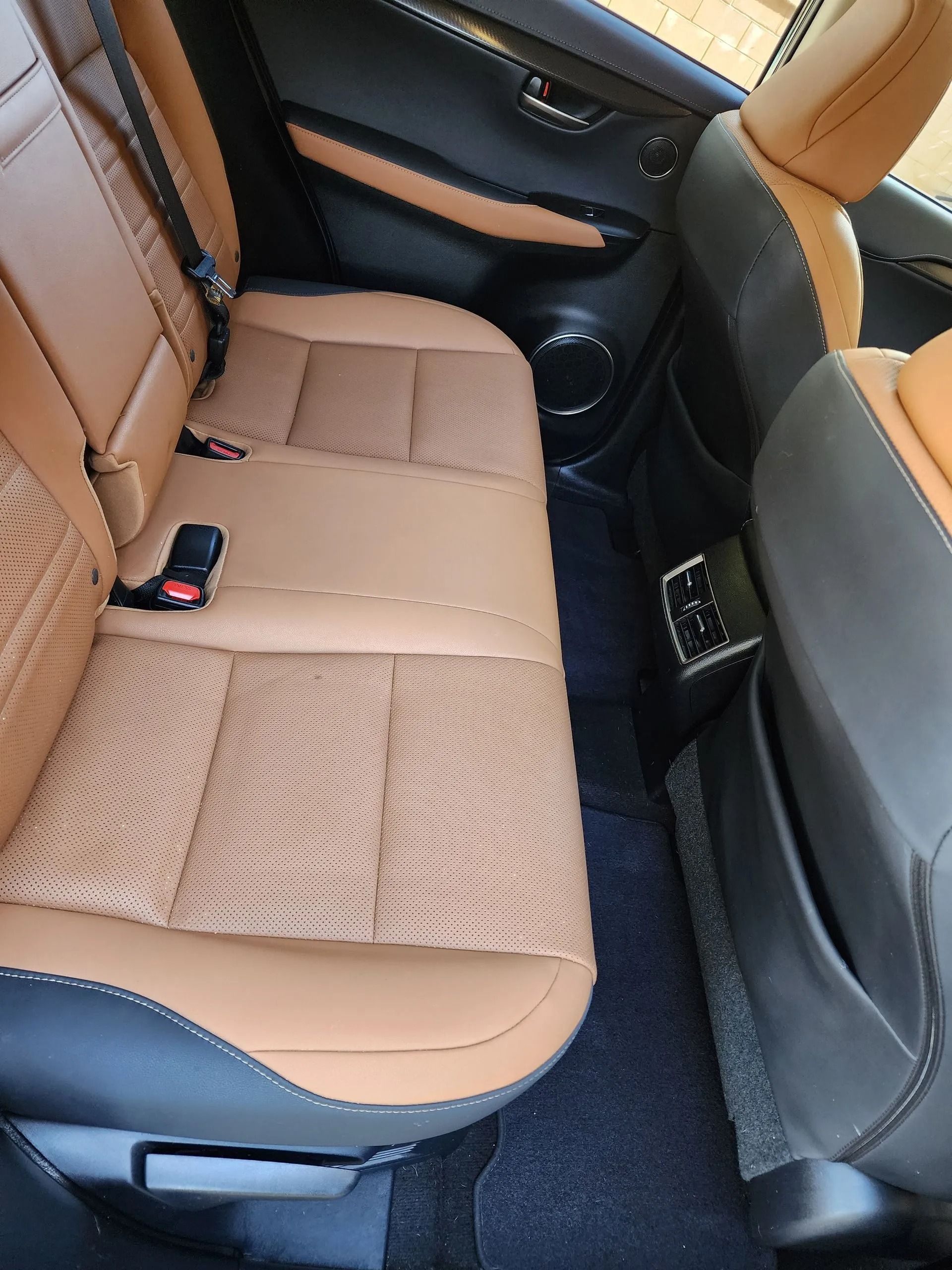 A close-up of a car's rear seat featuring two-tone tan and black leather upholstery with a perforated center pattern.