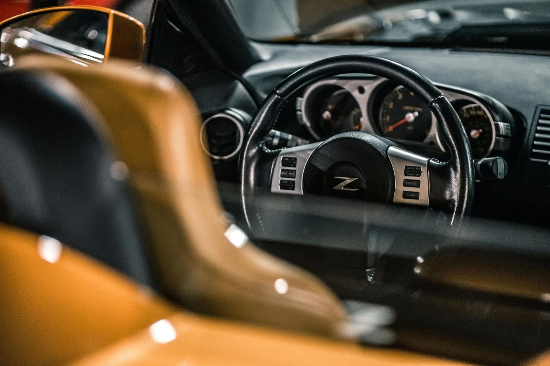 Interior view of a golden-yellow Nissan 350Z sports car, focusing on the steering wheel with the Z logo and dashboard.