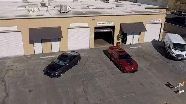 An aerial view of a single-story commercial building with a black car, red car, and white van parked in the lot.