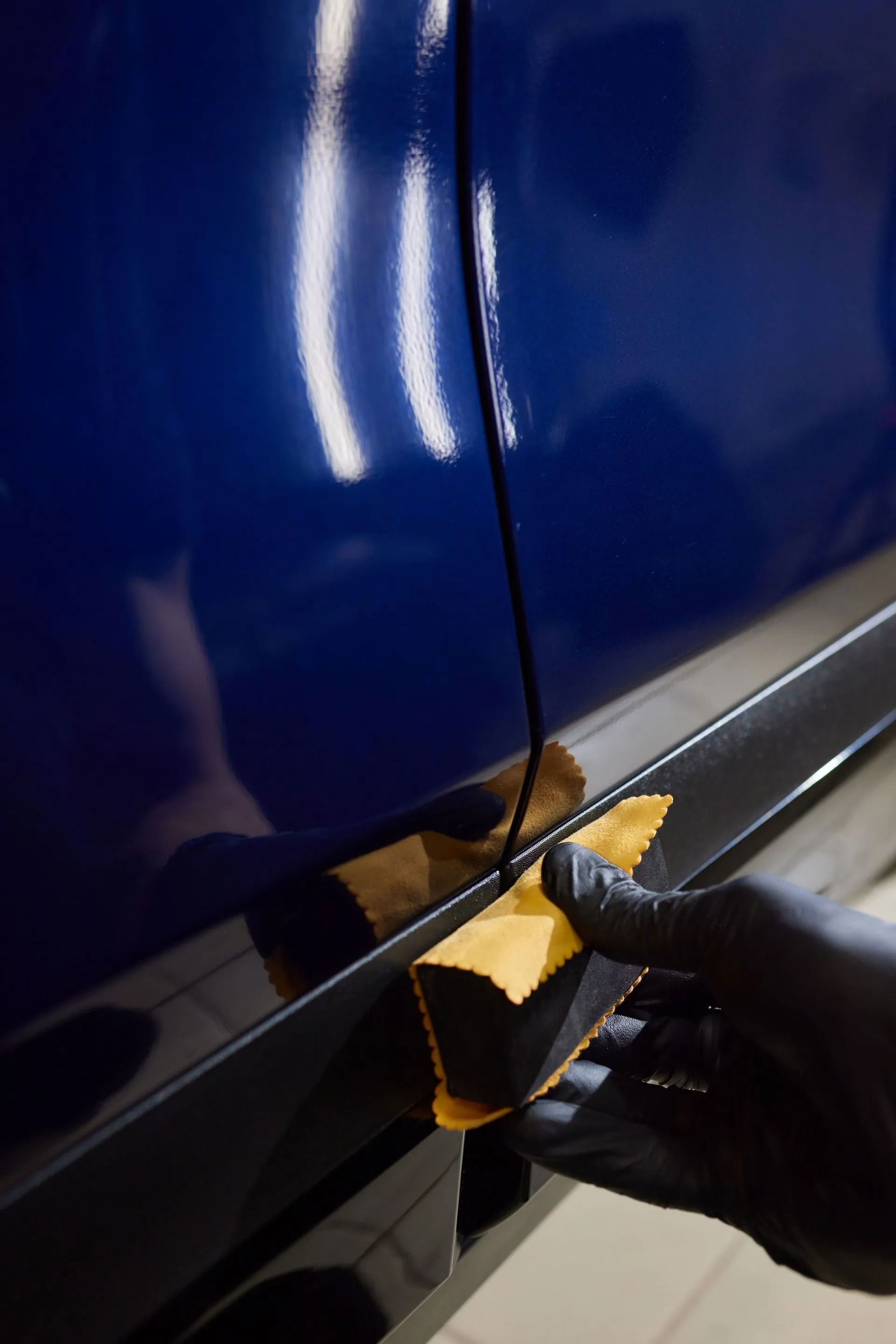 Gloved hand using an applicator sponge to apply ceramic coating to the side of a blue car.
