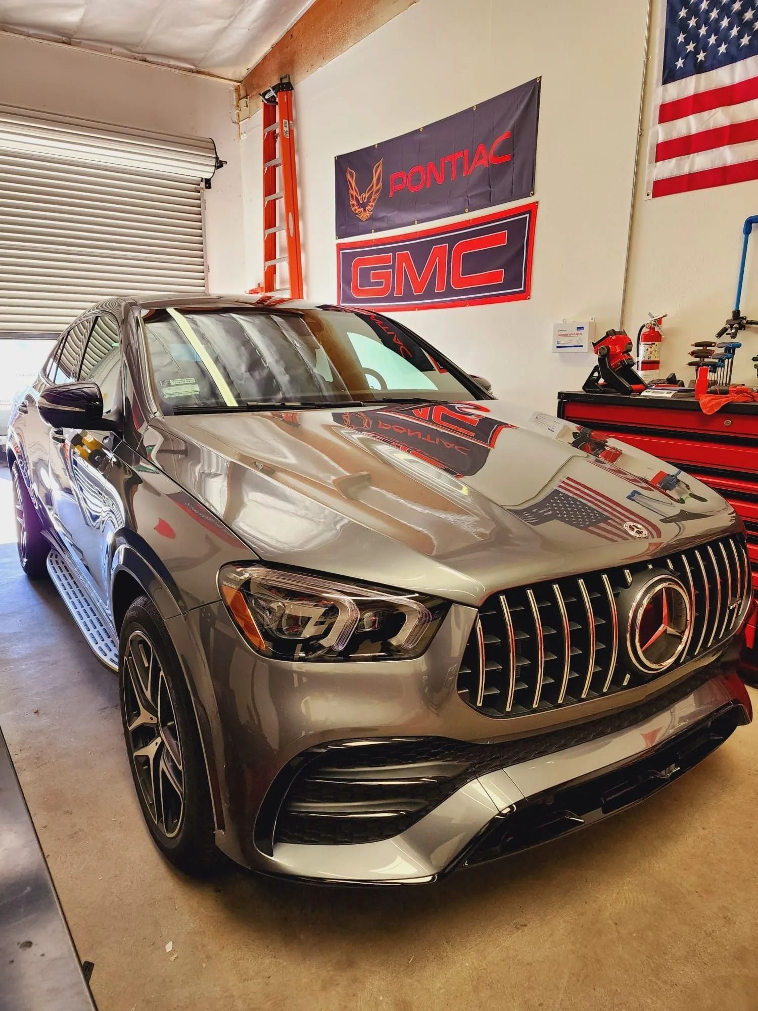 A gray Mercedes-Benz SUV parked in a garage with Pontiac and GMC signs on the wall.