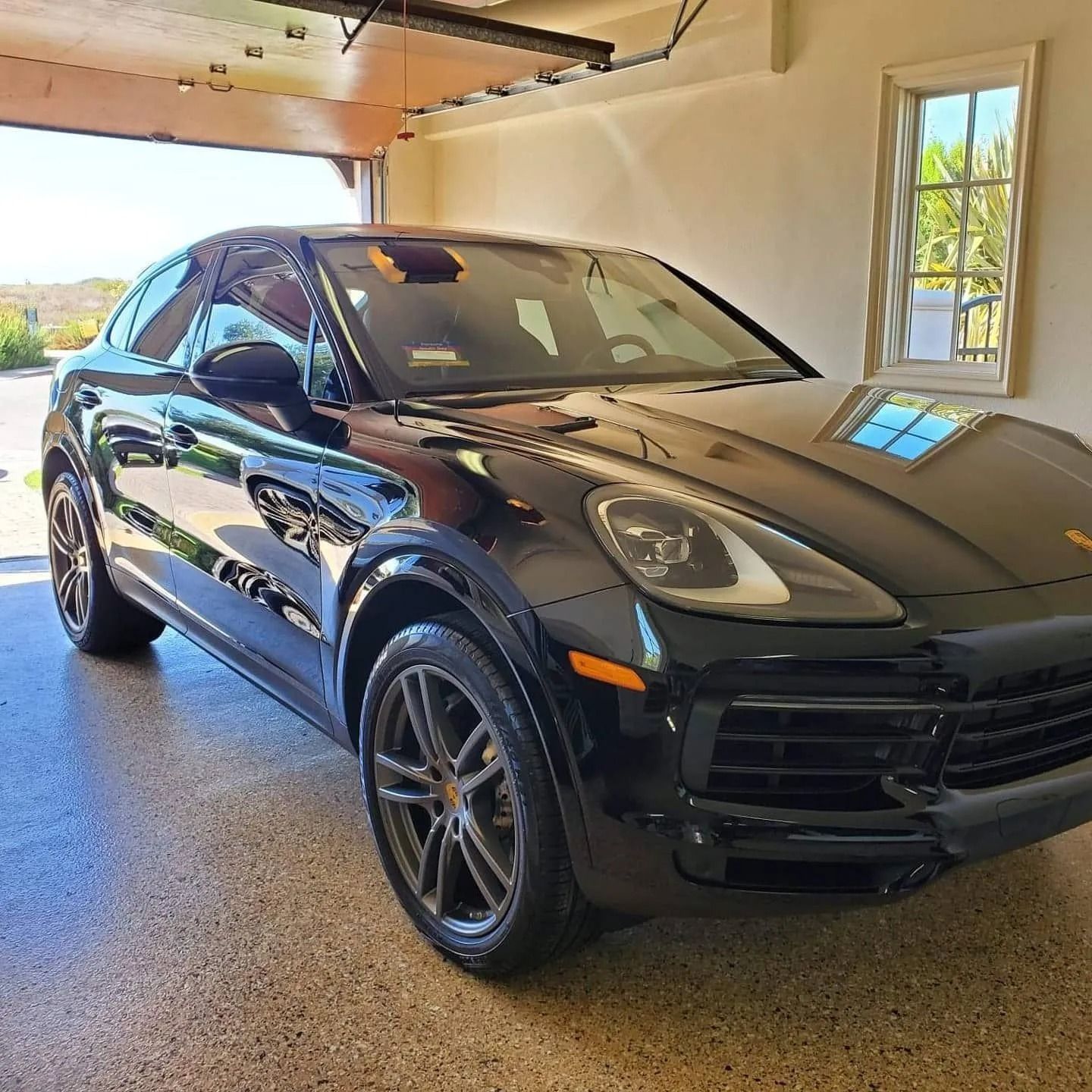 A black Porsche SUV parked inside a residential garage with an open door.