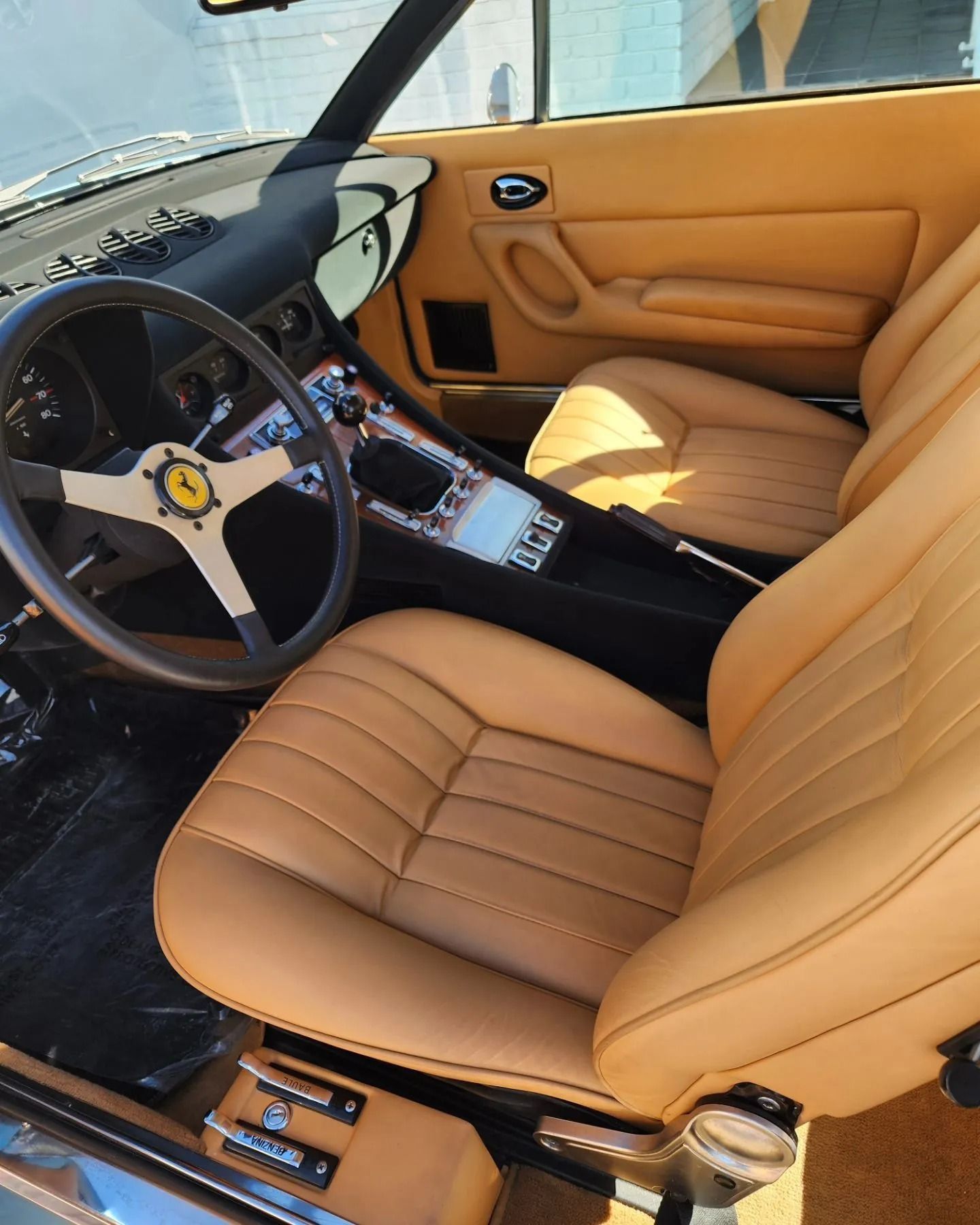 The tan leather interior of a vintage Ferrari, featuring a three-spoke steering wheel and a manual gear shifter.