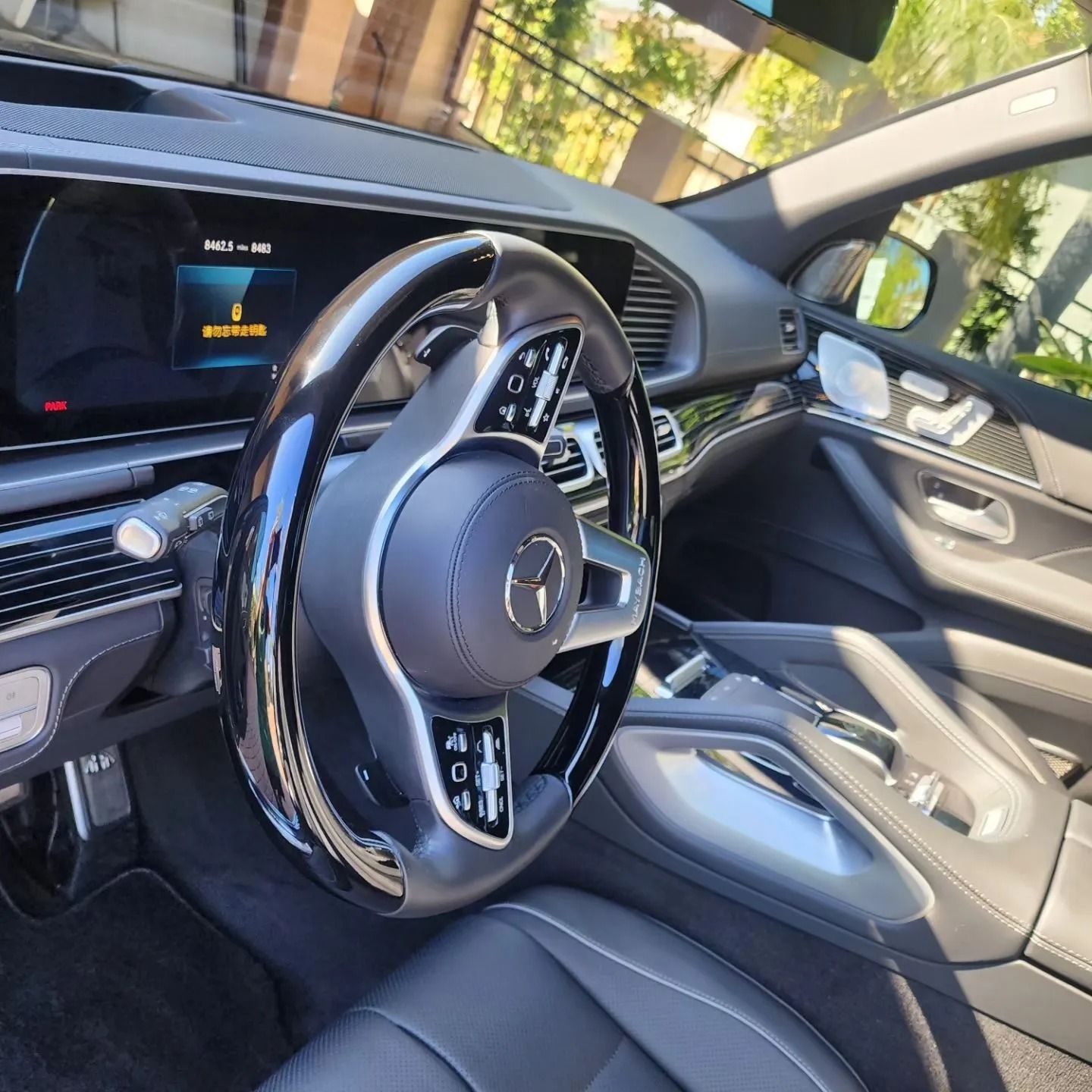 Interior of a Mercedes-Benz featuring a black leather and wood steering wheel, digital dashboard, and grey leather seating.