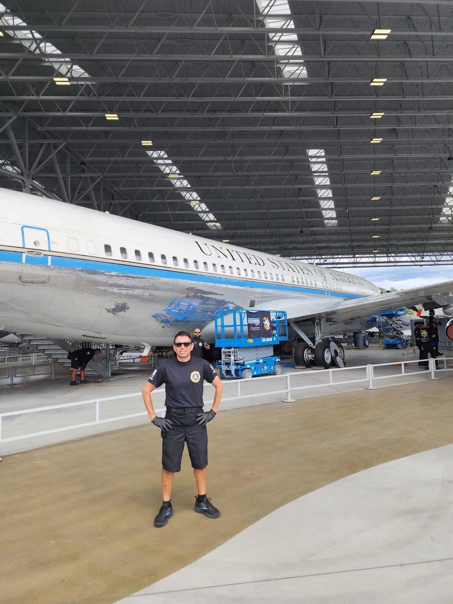 A person stands with hands on hips inside a hangar in front of a white aircraft marked 