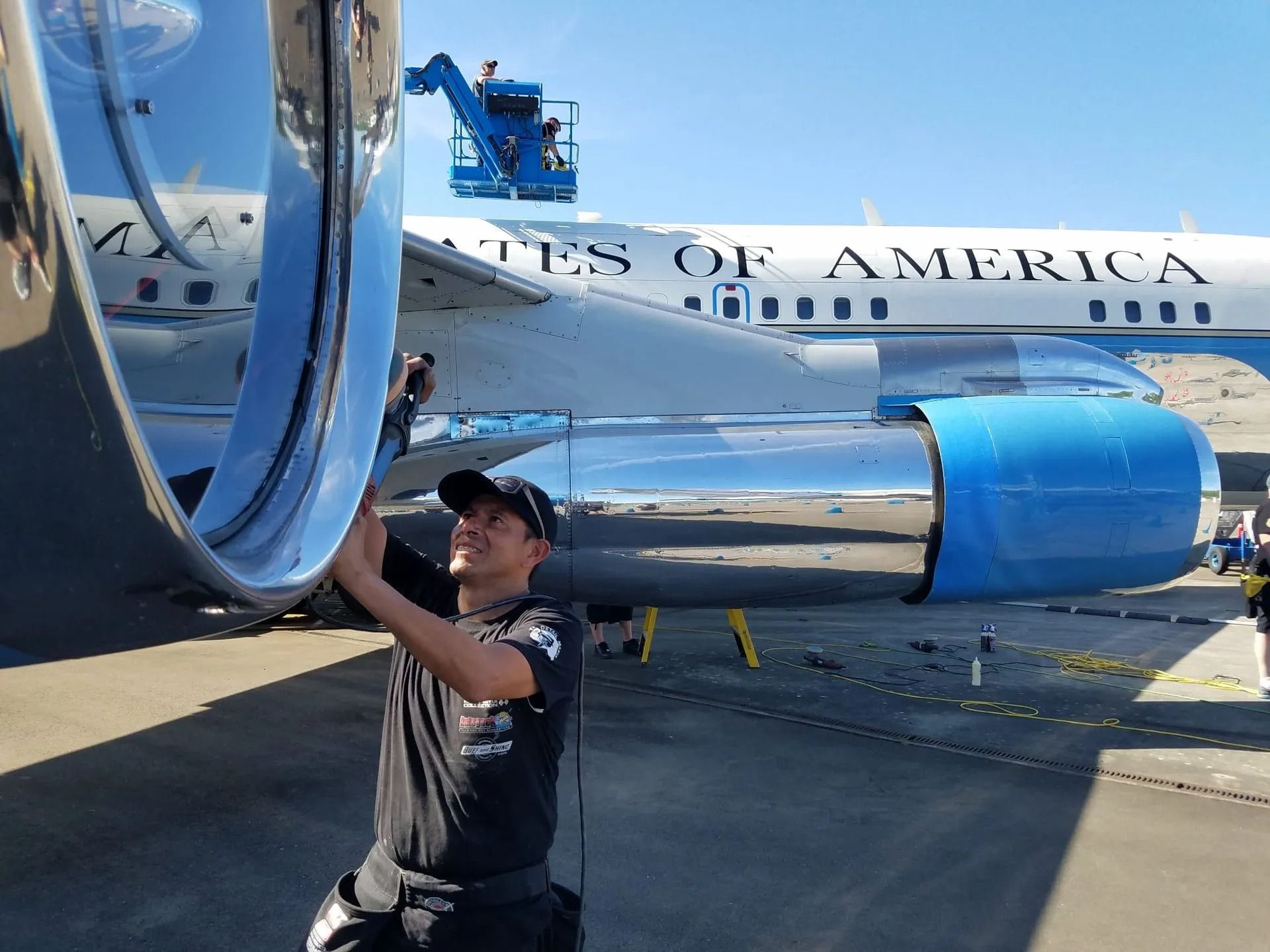 A technician smiles while inspecting the engine of a United States of America aircraft on an outdoor tarmac.